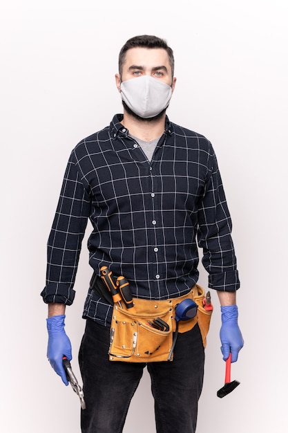 Jonge reparateur in vrijetijdskleding, beschermend masker en handschoenen die diy handgereedschap vasthoudt terwijl hij meubels of huis gaat repareren