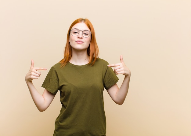 Jonge rode hoofd mooie vrouw die trots, positief en casual wijst naar de borst met beide handen