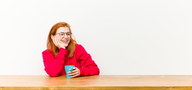 Jonge rode hoofd mooie vrouw voor een houten tafel met een koffiekopje