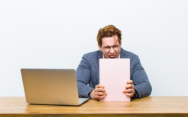 Jonge rode hoofdzakenman die in zijn bureau met een boek werkt