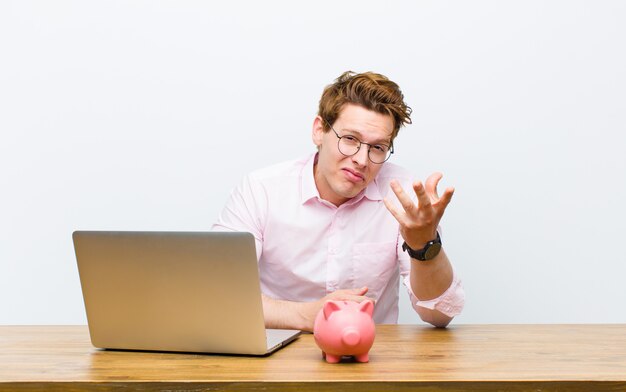 Jonge rode hoofdzakenman die in zijn bureau met een spaarvarken werkt