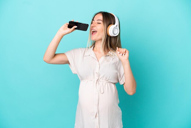 Jonge Roemeense vrouw geïsoleerd op blauwe achtergrond zwanger en dansen tijdens het luisteren naar muziek