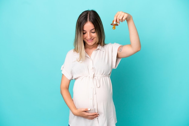 Jonge Roemeense vrouw geïsoleerd op blauwe achtergrond zwanger en met een fopspeen