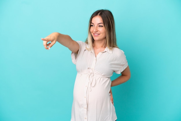 Jonge Roemeense vrouw geïsoleerd op blauwe achtergrond zwanger en wijzend naar voren