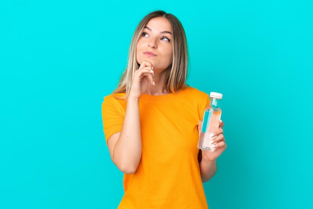 Jonge Roemeense vrouw met een fles water geïsoleerd op blauwe achtergrond en opzoeken