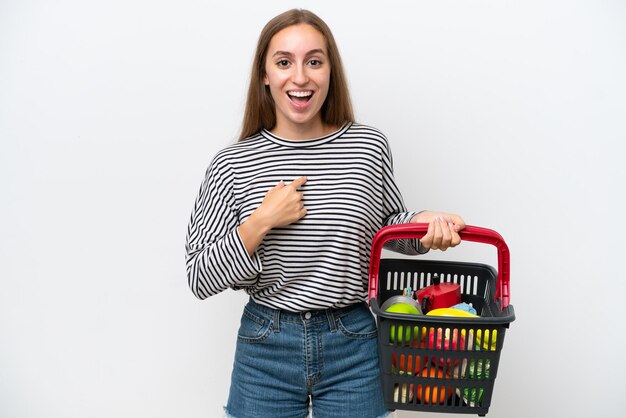 Jonge Roemeense vrouw met een winkelmandje vol voedsel geïsoleerd op een witte achtergrond met verrassende gezichtsuitdrukking