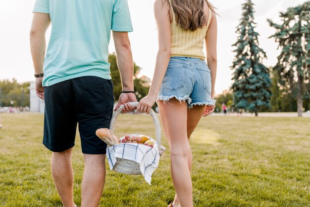 Jonge romantische de picknickmand van de paarholding met vruchten in het park