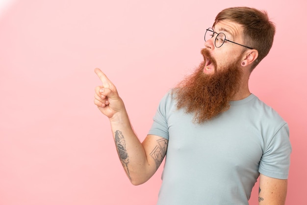 Jonge roodachtige blanke man geïsoleerd op roze achtergrond die van plan is de oplossing te realiseren terwijl hij een vinger opheft