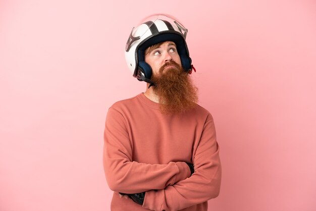 Jonge roodachtige blanke man met een motorhelm geïsoleerd op roze achtergrond en opzoeken