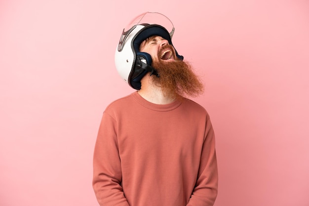 Jonge roodachtige blanke man met een motorhelm geïsoleerd op roze achtergrond lachen