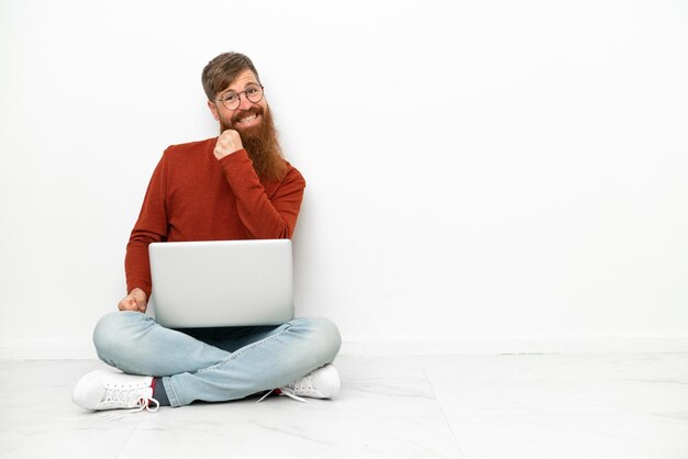 Jonge roodachtige blanke man met laptop geïsoleerd op een witte achtergrond die een overwinning viert