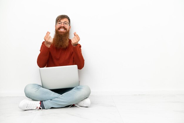 Foto jonge roodachtige blanke man met laptop geïsoleerd op een witte achtergrond geld gebaar maken