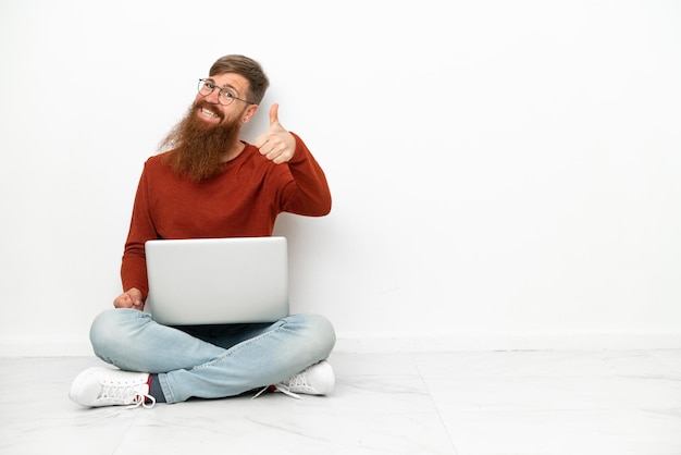 Jonge roodachtige blanke man met laptop geïsoleerd op een witte achtergrond met duimen omhoog omdat er iets goeds is gebeurd