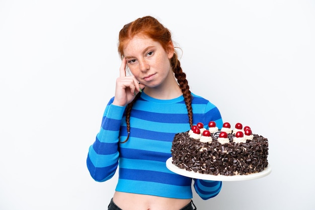 Jonge roodachtige vrouw met verjaardagstaart geïsoleerd op een witte achtergrond denken een idee