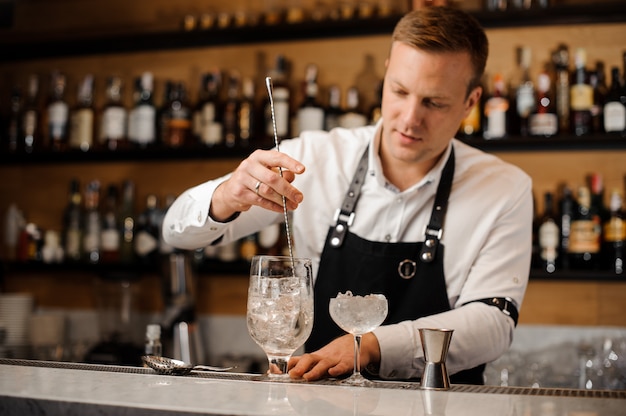 Jonge roodharige barman roeren alcoholische drank met ijsblokjes