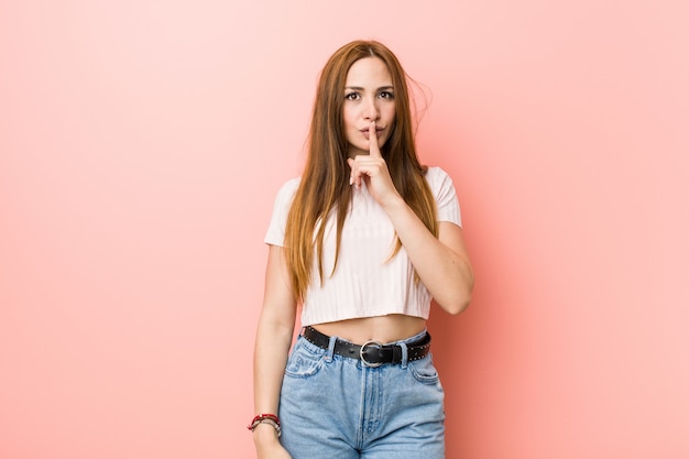 Jonge roodharige gembervrouw tegen een roze muur die een geheim houdt