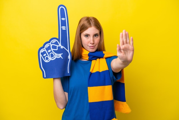 Jonge roodharige sportfan vrouw geïsoleerd op gele achtergrond stop gebaar maken