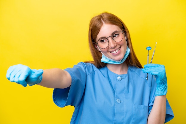 Jonge roodharige tandarts vrouw geïsoleerd op gele achtergrond met een duim omhoog gebaar