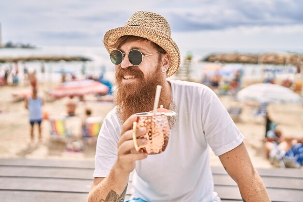 Jonge roodharige toeristische man cocktail drinken zittend op de bank op het strand