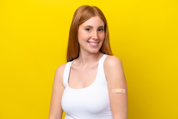 Jonge roodharige vrouw die een bandaids draagt die op gele achtergrond met gelukkige uitdrukking wordt geïsoleerd