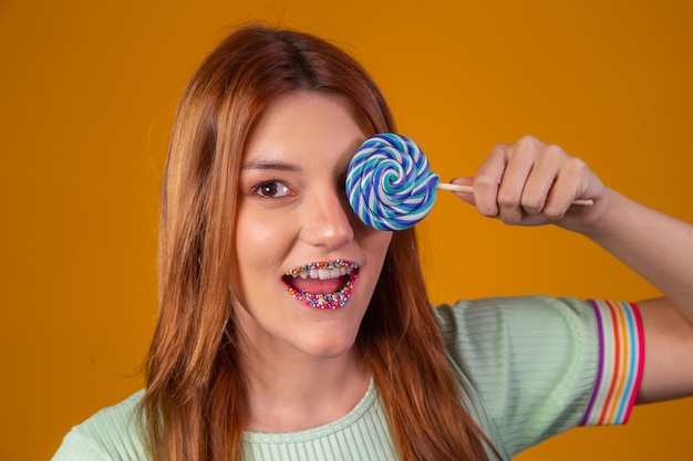 Jonge roodharige vrouw die één oog bedekt met een blauwe lolly en een gekleurde mond.