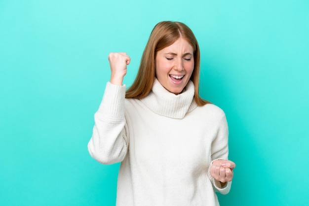 Jonge roodharige vrouw geïsoleerd op een blauwe achtergrond die een overwinning viert