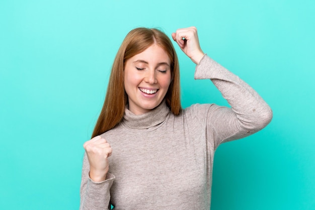 Jonge roodharige vrouw geïsoleerd op een blauwe achtergrond die een overwinning viert