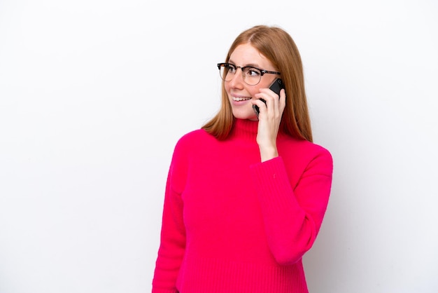 Jonge roodharige vrouw geïsoleerd op een witte achtergrond die een gesprek houdt met de mobiele telefoon met iemand