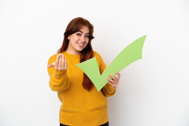 Jonge roodharige vrouw geïsoleerd op een witte achtergrond die een vinkje houdt en een komend gebaar doet