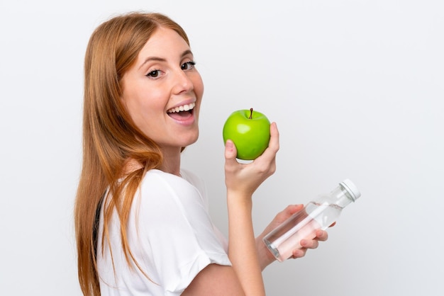 Jonge roodharige vrouw geïsoleerd op een witte achtergrond met een appel en met een fles water