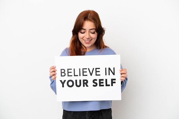 Jonge roodharige vrouw geïsoleerd op een witte achtergrond met een bordje met de tekst Believe In Your Self