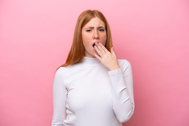 Foto jonge roodharige vrouw geïsoleerd op roze achtergrond geeuwen en wijd open mond met hand bedekken