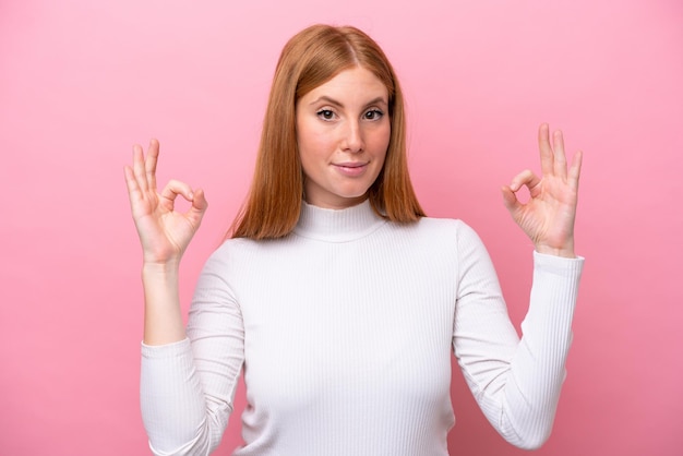 Jonge roodharige vrouw geïsoleerd op roze achtergrond in zen pose