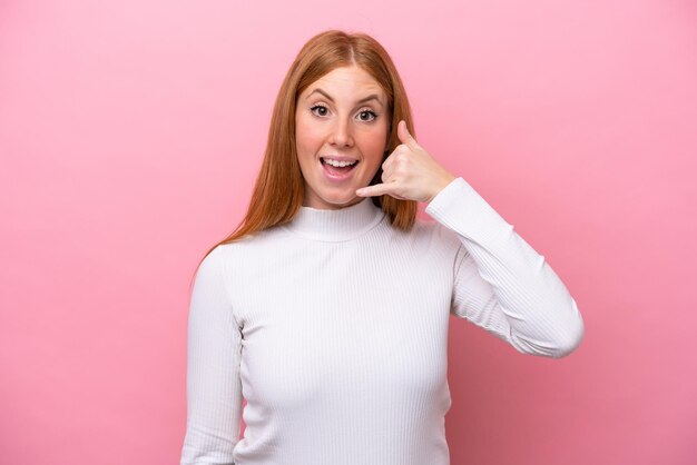 Jonge roodharige vrouw geïsoleerd op roze achtergrond telefoon gebaar maken Bel me terug teken