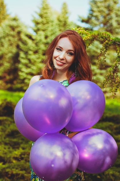 jonge roodharige vrouw in de lentetuin met sproeten. Paarse ballonnen. Verjaardag, vakantieviering.