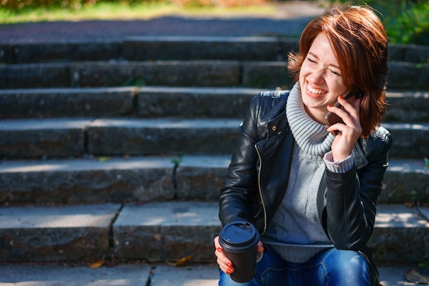 Jonge roodharige vrouw in een leren jas praten aan de telefoon buitenshuis.