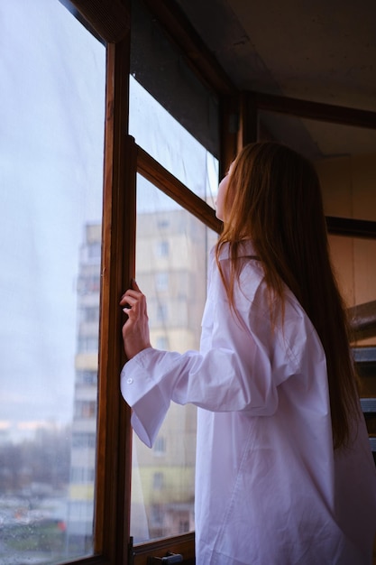 Jonge roodharige vrouw in wit shirt kijkt uit het raam op het balkon diep in gedachten roodharig gember meisje algemeen vliegtuig