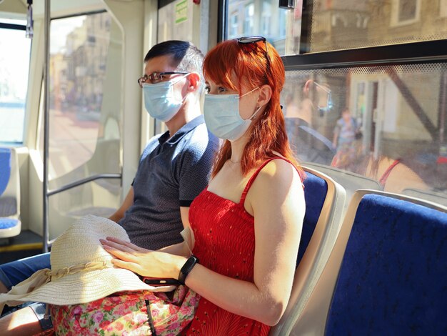 Jonge roodharige vrouw met een beschermend gezichtsmasker zit naast de man in het openbaar vervoer