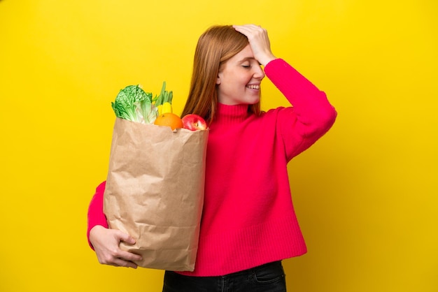 Jonge roodharige vrouw met een boodschappentas geïsoleerd op een gele achtergrond heeft iets gerealiseerd en is van plan de oplossing