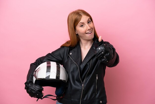 Jonge roodharige vrouw met een motorhelm geïsoleerd op roze achtergrond met duimen omhoog omdat er iets goeds is gebeurd