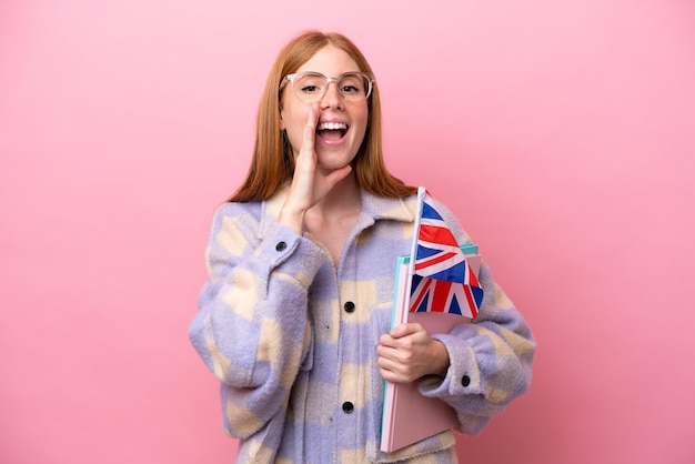 Jonge roodharige vrouw met een vlag van het Verenigd Koninkrijk geïsoleerd op roze achtergrond schreeuwend met wijd open mond
