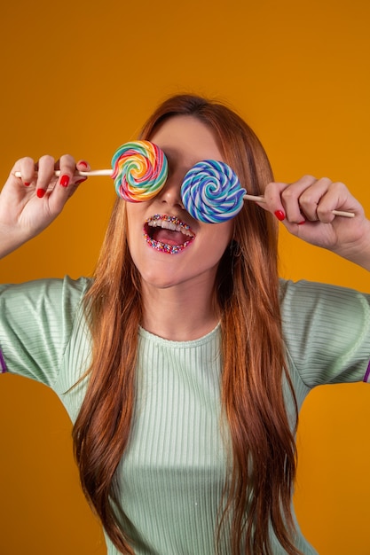 Jonge roodharige vrouw met kleurrijke lolly's die haar ogen blinddoeken. mode concept