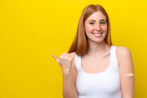 Jonge roodharige vrouw met pleisters geïsoleerd op een gele achtergrond die naar de zijkant wijst om een product te presenteren