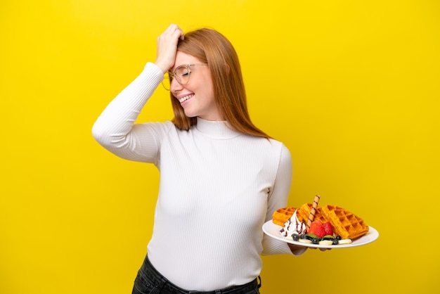 Jonge roodharige vrouw met wafels geïsoleerd op een gele achtergrond heeft iets gerealiseerd en is van plan de oplossing te vinden