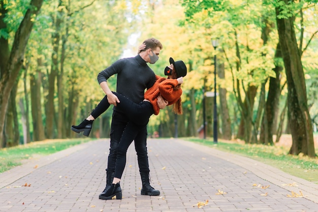 Jonge roodharige vrouw zet op een gezichtsmasker tijdens het wandelen met jonge man in herfst park