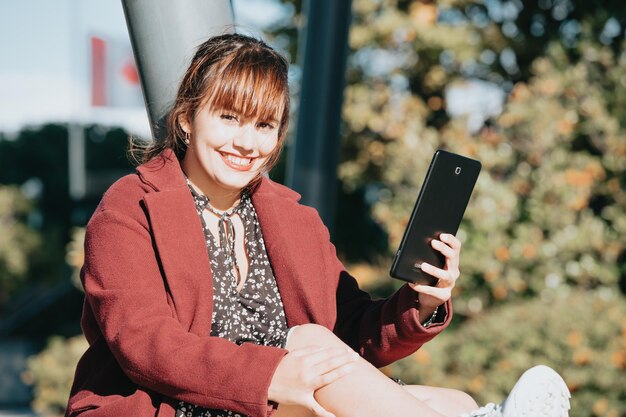 Jonge roodharige zakenvrouw lacht naar de camera terwijl ze de tablet buiten kantoor gebruikt. kopieer ruimtebeeld, zaken en werk op kantoor. buiten het kantoor, elegante trendy look