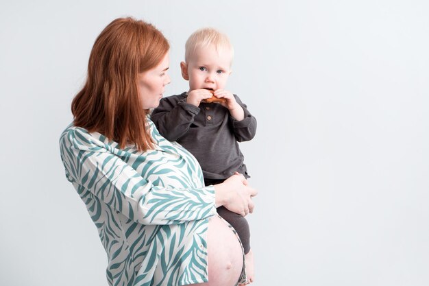 jonge roodharige zwangere vrouw in pyjama met 15-jarige zoon in haar armen