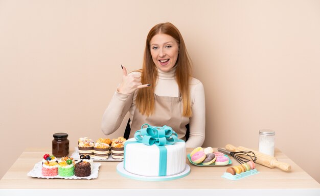 Jonge roodharigevrouw met een grote cake die telefoongebaar maakt