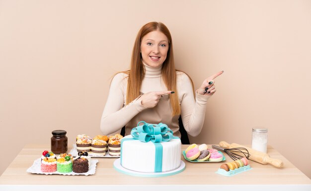 Jonge roodharigevrouw met een grote cake die vinger aan de kant richt