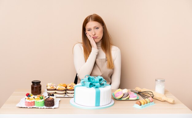 Jonge roodharigevrouw met een grote cake ongelukkig en gefrustreerd